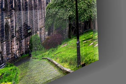 Angled view of glass wall art showing ivy-covered stone cathedral walls with green lawn and black lamp post in foreground.