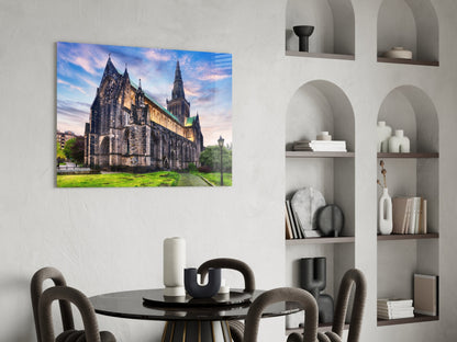 Glass wall art print of Glasgow Cathedral at dusk displayed above a black dining table in a minimalist interior setting.
