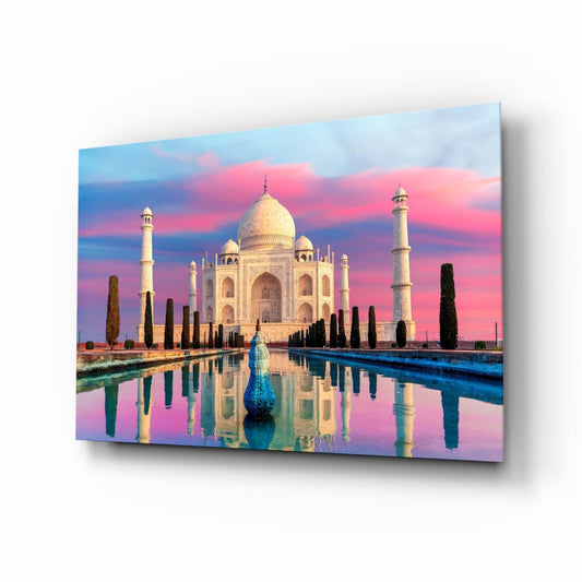 Glass wall art displaying the Taj Mahal at sunset reflected in still water, with pink and blue sky, cypress trees, and a peacock sculpture.