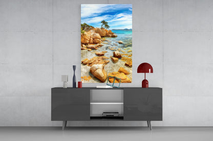 Beach wall art glass panel mounted above dark gray media console, displaying rocky coastline with turquoise water and blue sky.
