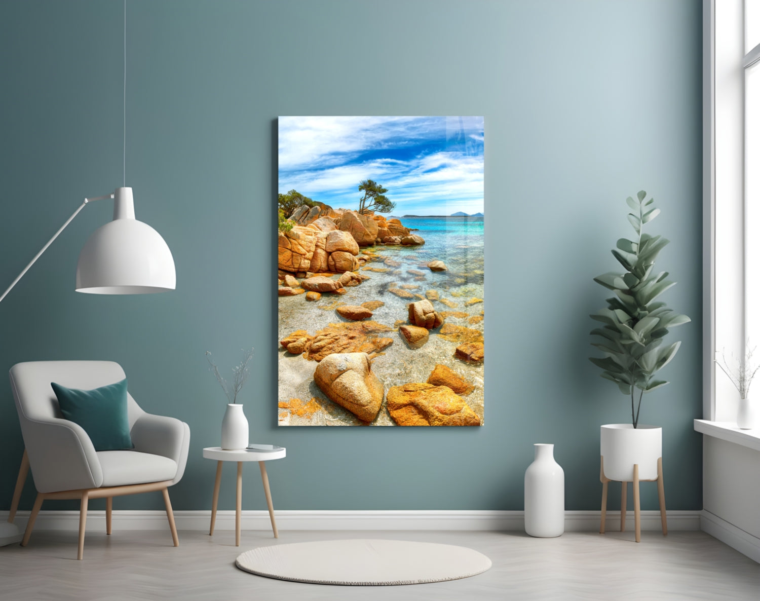 Beach landscape glass wall art depicting golden rocks, turquoise water, and pine tree displayed in modern living room.