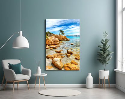 Beach landscape glass wall art depicting golden rocks, turquoise water, and pine tree displayed in modern living room.