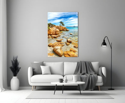 Beach View Glass Wall Art displayed above white sofa showing rocky coastline with turquoise water and blue sky.