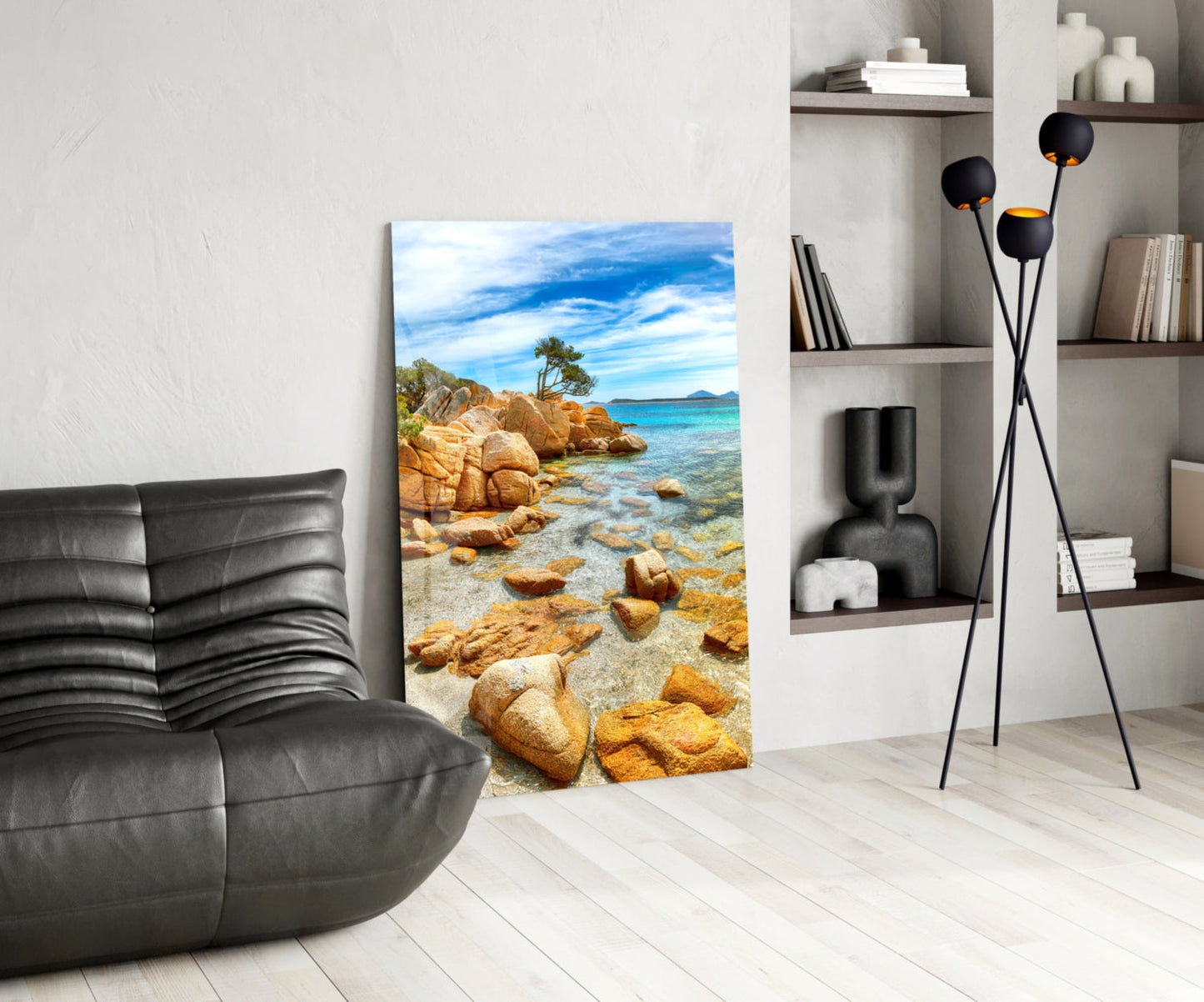 Beach view glass wall art displayed in modern living room with black leather chair, shelving unit, and floor lamp.
