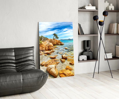 Beach view glass wall art displayed in modern living room with black leather chair, shelving unit, and floor lamp.