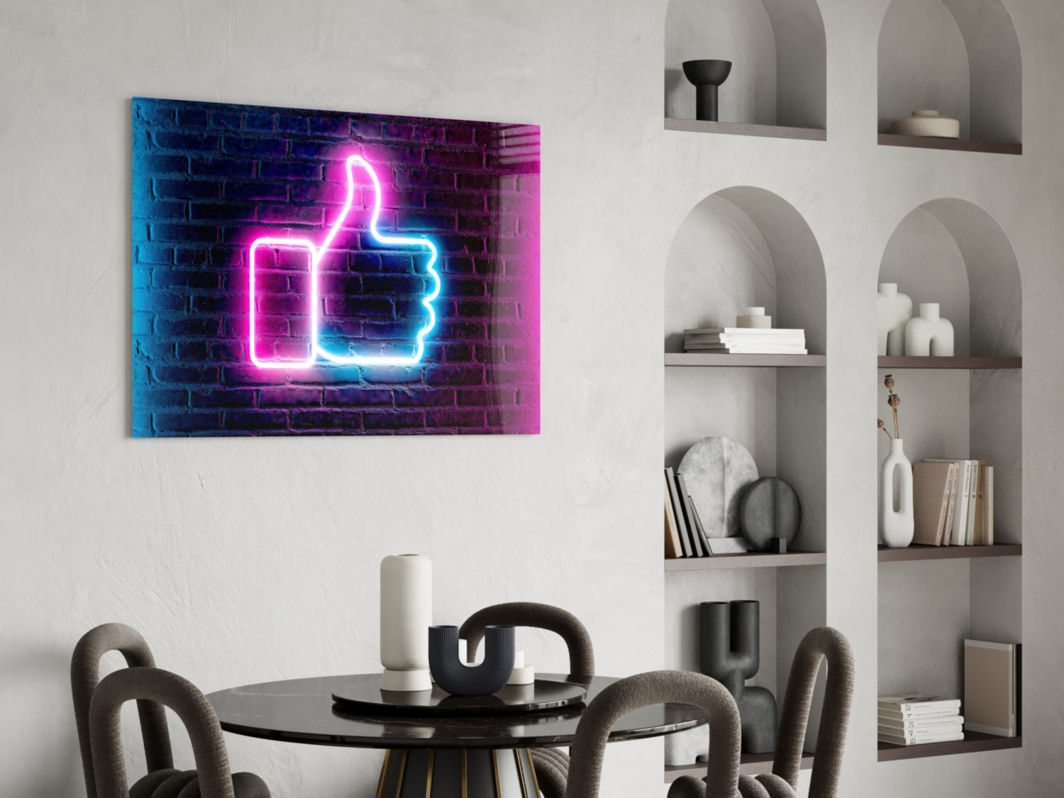Neon thumbs-up sign in pink and blue mounted on brick wall above dining table with chairs and shelving unit.