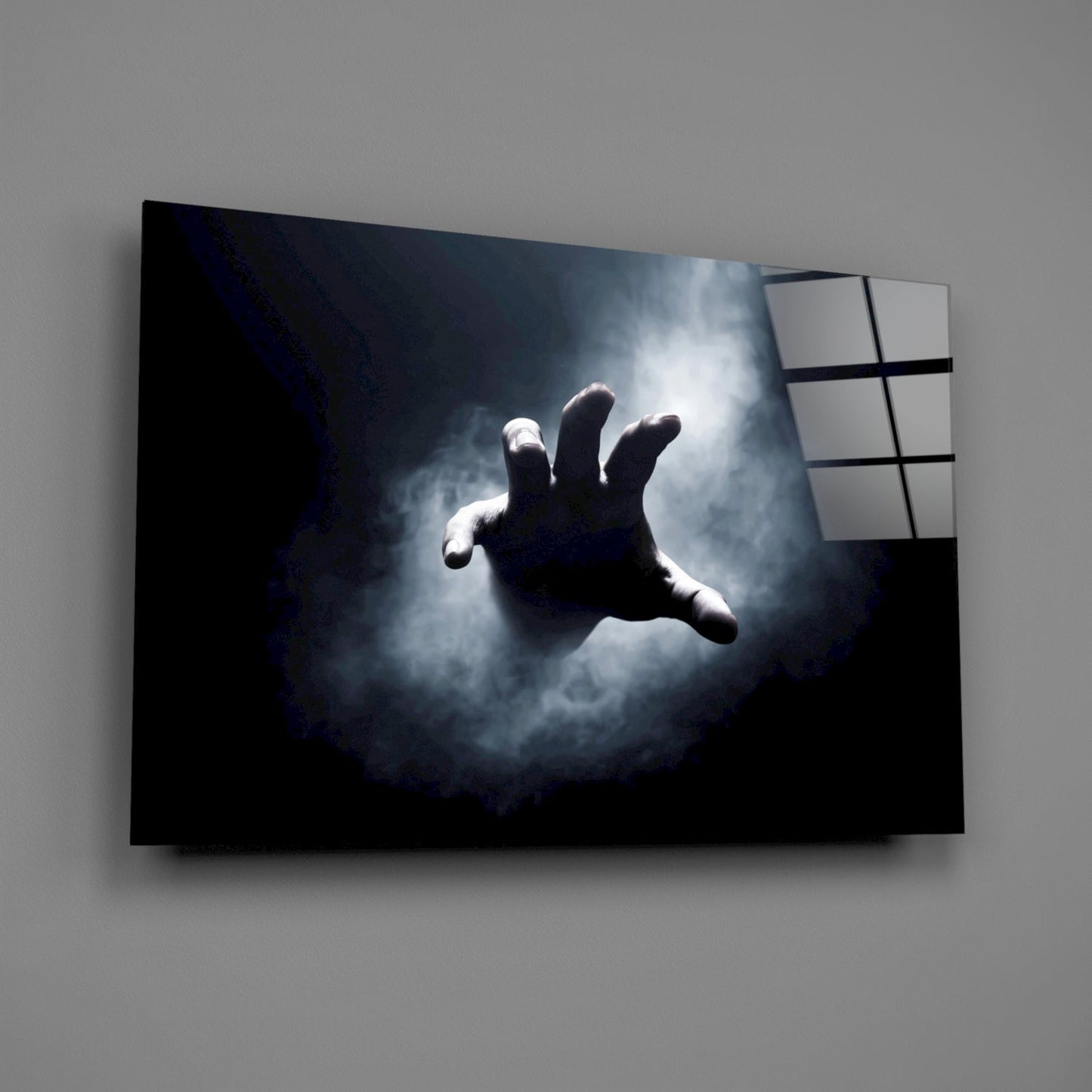 Glass wall art panel mounted at an angle displaying a silhouetted hand reaching toward light through stormy clouds.