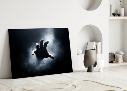 Dark glass wall art depicting a silhouetted hand reaching upward against stormy sky, leaning against white interior wall with shelving.