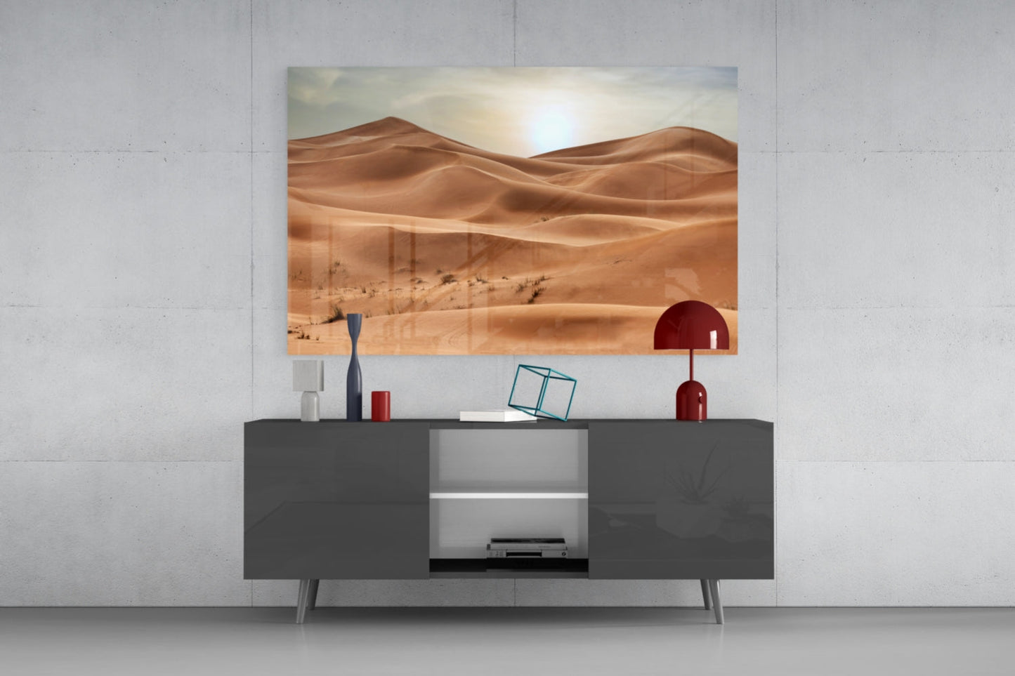 Desert landscape glass wall art displaying golden sand dunes and sun, mounted above dark gray media console with decorative accessories.