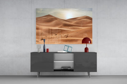 Desert landscape glass wall art displaying golden sand dunes and sun, mounted above dark gray media console with decorative accessories.