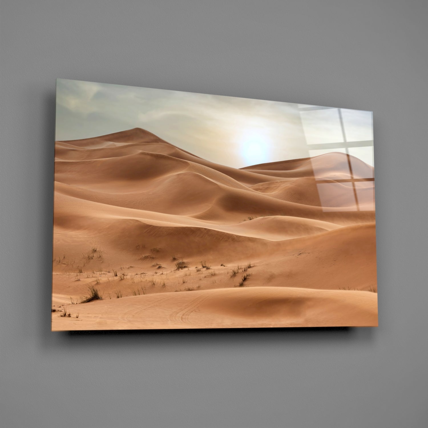 Glass wall art depicting golden sand dunes under bright sunlight with scattered desert vegetation and window reflections.