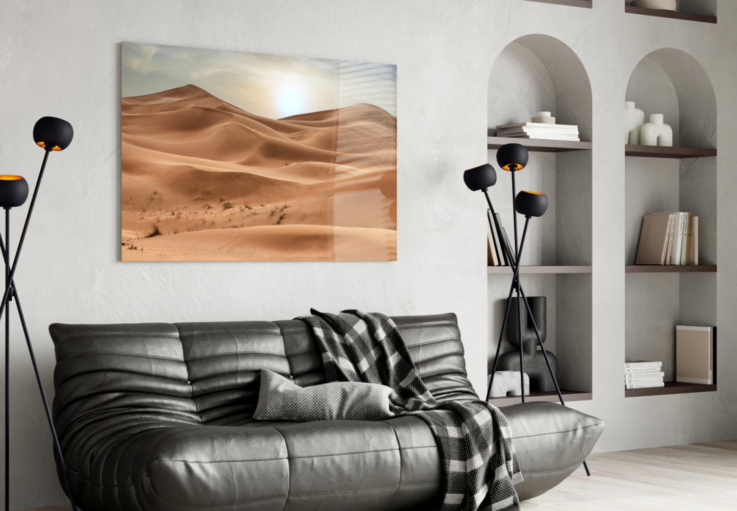 Desert landscape glass wall art depicting golden sand dunes and sun, displayed above black leather sofa in modern living room interior.