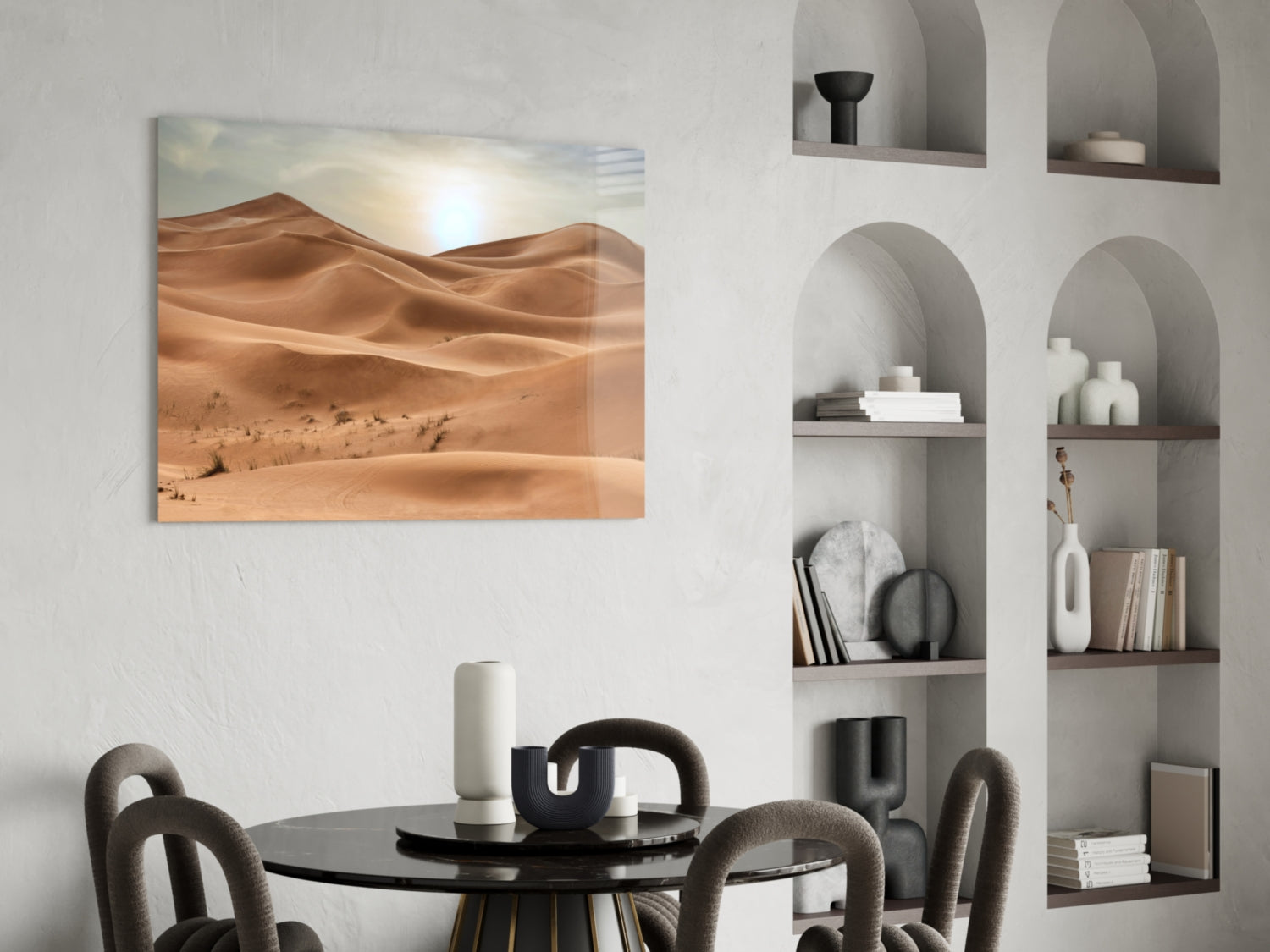 Glass wall art depicting golden sand dunes under bright sunlight, displayed above a black dining table in a minimalist interior setting.