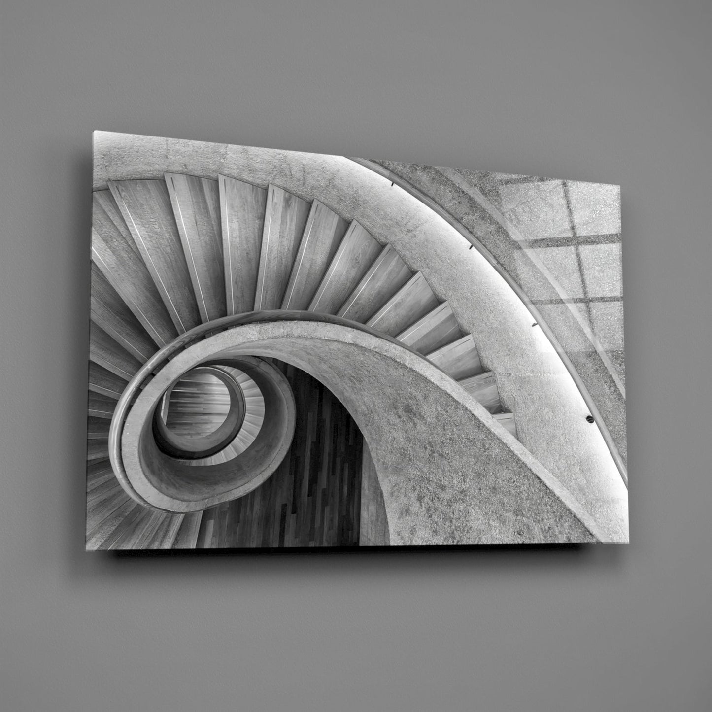 Monochrome photograph of a spiral staircase viewed from above, showing concentric circular steps and concrete walls descending into darkness.