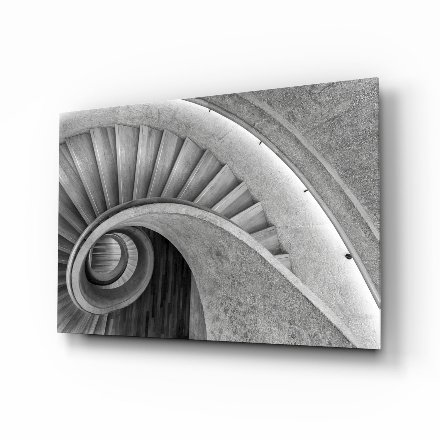 Black and white photograph of a spiral staircase viewed from above, showing concentric circular steps and handrails in concrete.