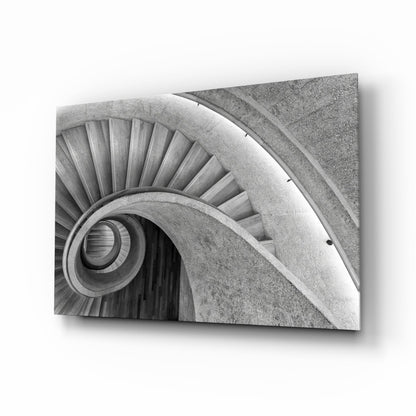 Black and white photograph of a spiral staircase viewed from above, showing concentric circular steps and handrails in concrete.
