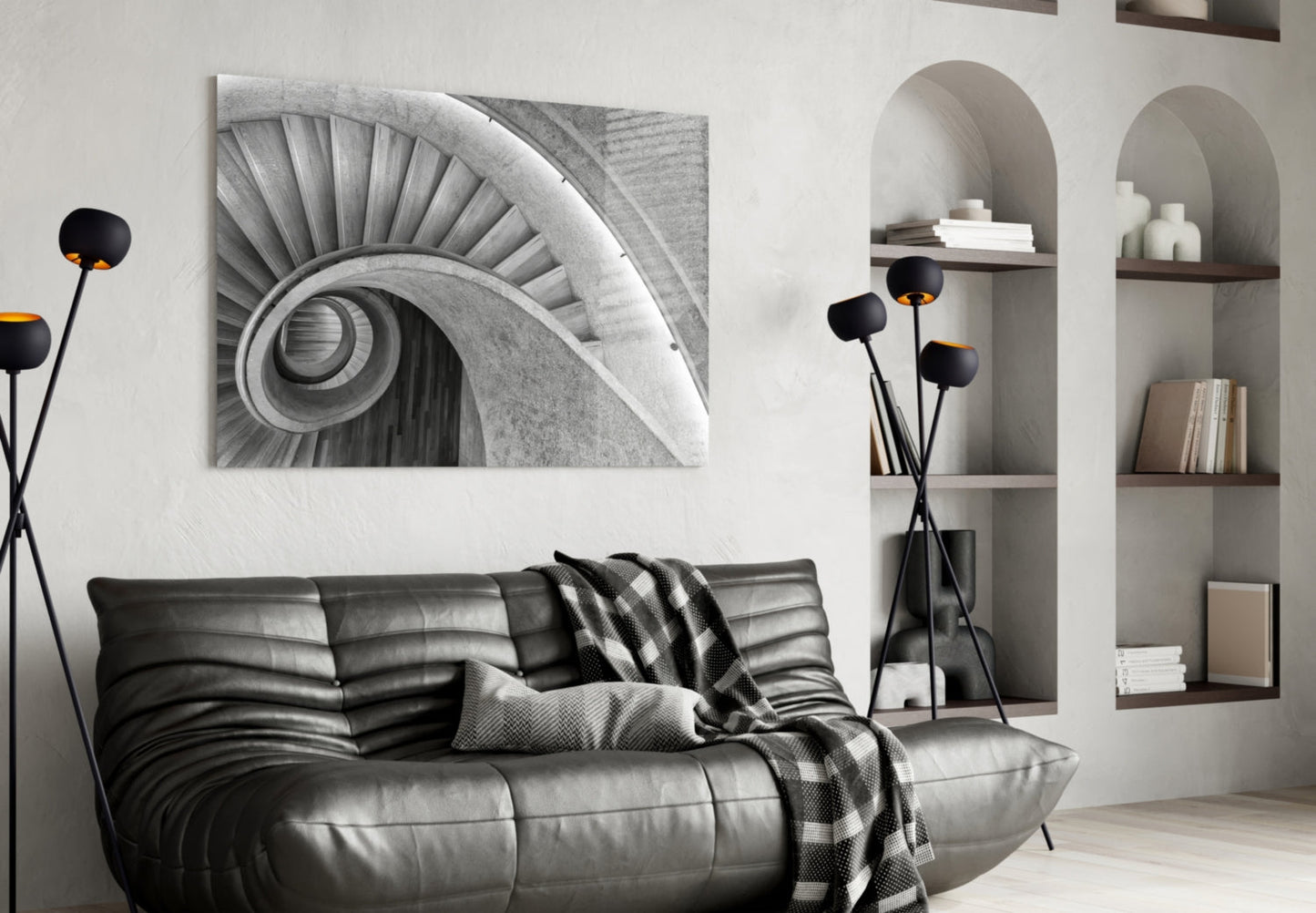 Black and white architectural photograph of a spiral staircase displayed above a gray leather sofa in a modern living room.