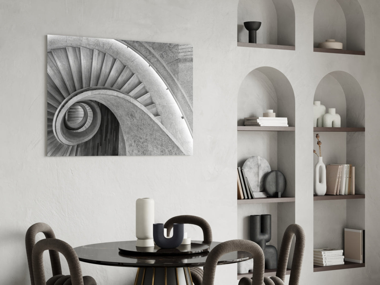 Black and white architectural glass wall art depicting a spiral staircase hung above a round black dining table with upholstered chairs.
