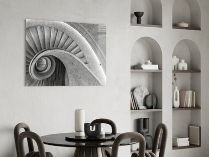 Black and white architectural glass wall art depicting a spiral staircase hung above a round black dining table with upholstered chairs.