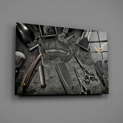 Black and white overhead arrangement of barber tools including scissors, clippers, combs, and brushes on textured gray surface displayed on glass wall art.