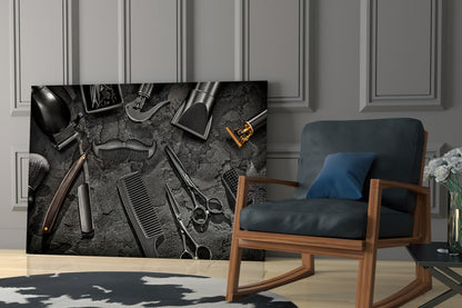 Black and white glass wall art displaying professional barbering tools arranged on textured surface, installed in modern room with wooden chair.