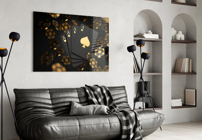Black glass wall art with gold playing cards and dice displayed above gray leather sofa in modern living room setting.