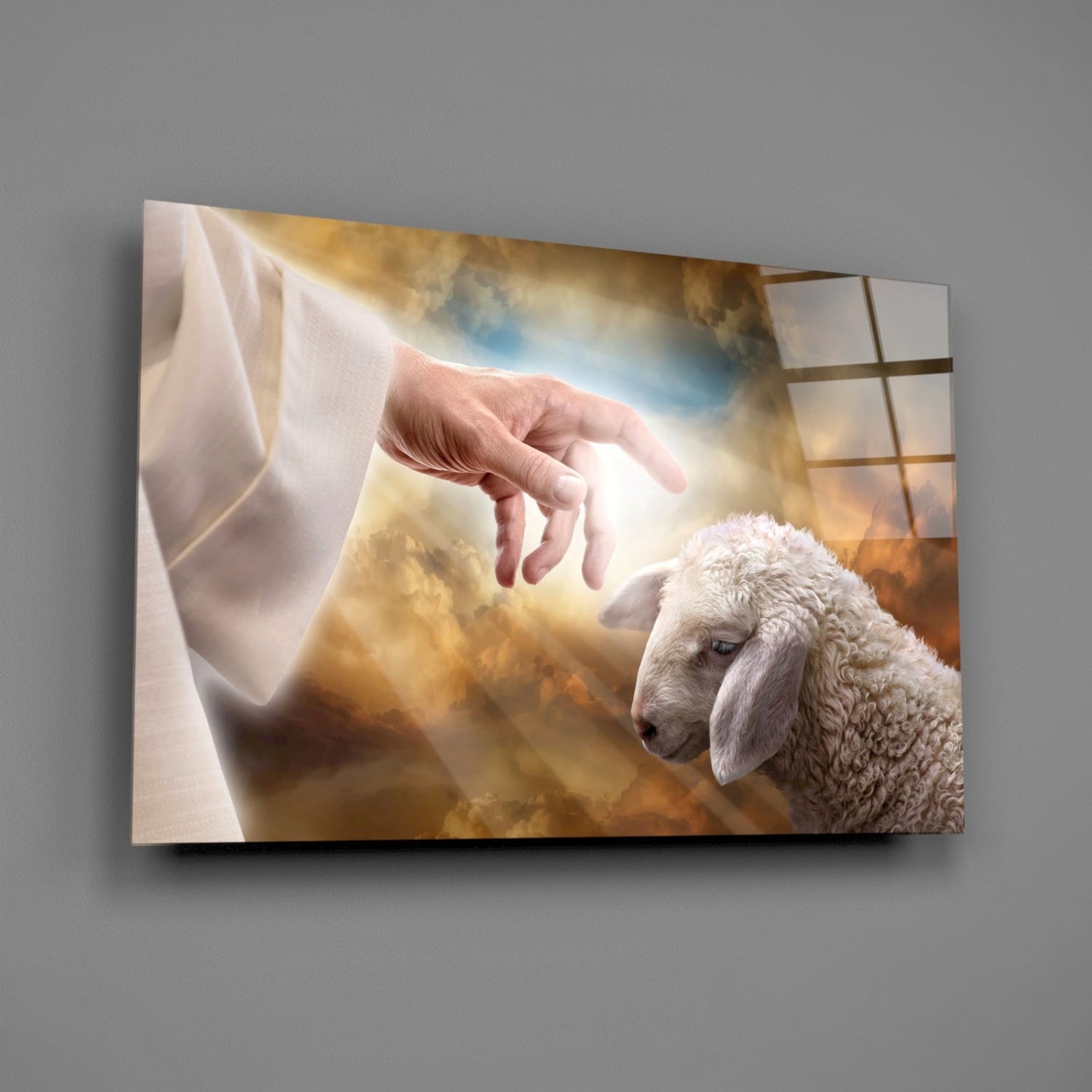 Glass wall art displaying a divine hand reaching toward a white lamb against a golden cloudy sky background.