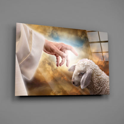 Glass wall art displaying a divine hand reaching toward a white lamb against a golden cloudy sky background.