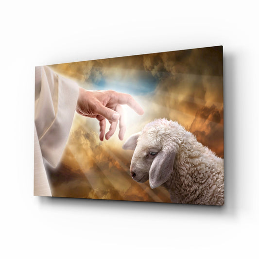 Glass wall art depicting a divine hand reaching toward a white lamb against a dramatic golden and blue cloudy sky background.