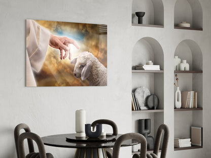 Glass wall art depicting a hand reaching toward a white lamb against golden clouds, displayed above a black dining table in a modern interior.