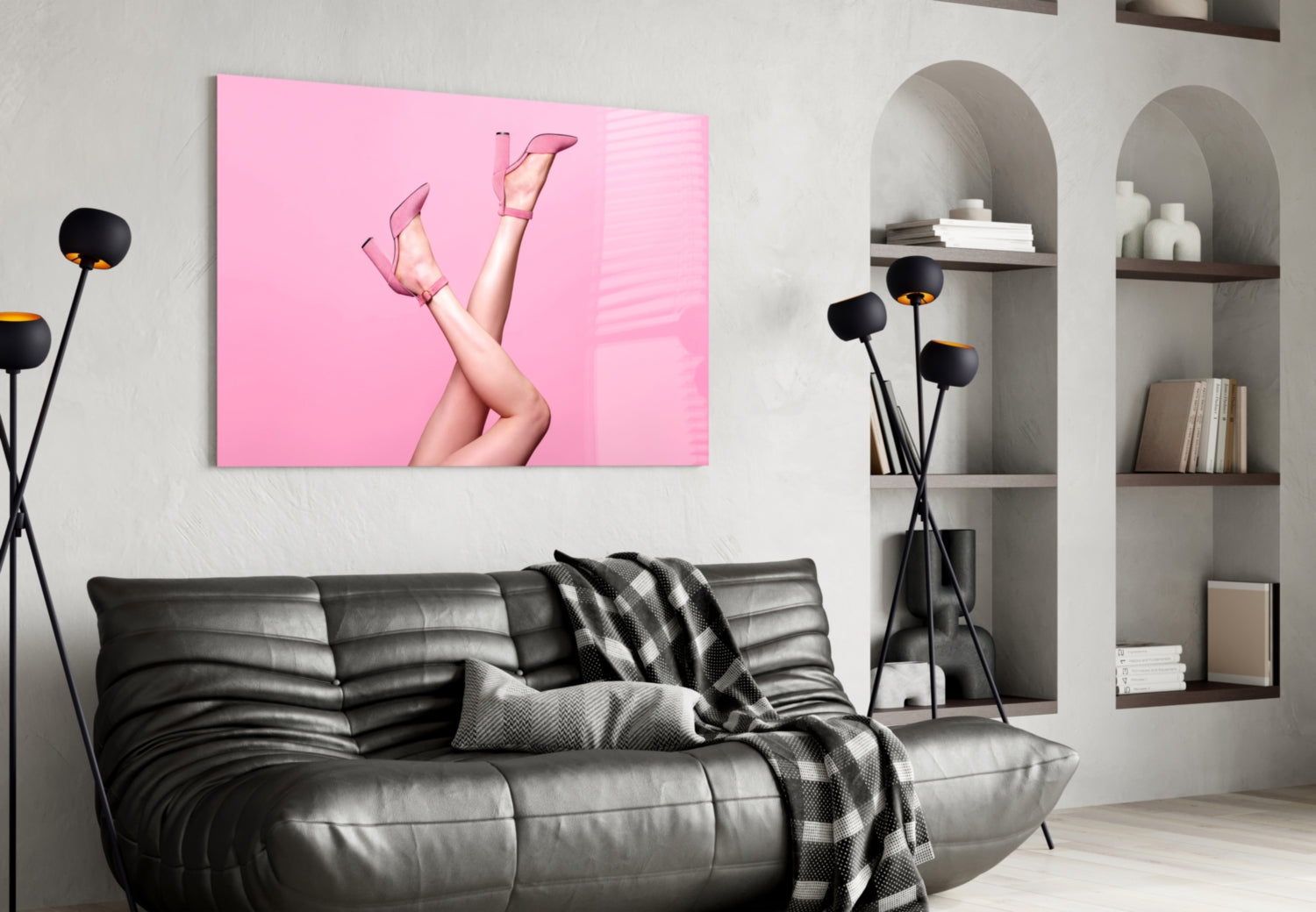 Pink glass wall art featuring a woman's legs in pink heels against a bright pink background, displayed above a black leather sofa.