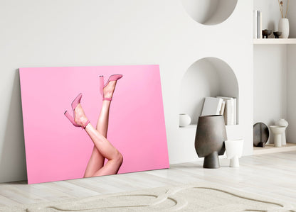 Pink glass wall art leaning against white wall displays woman's legs in pink heels against bright pink background.