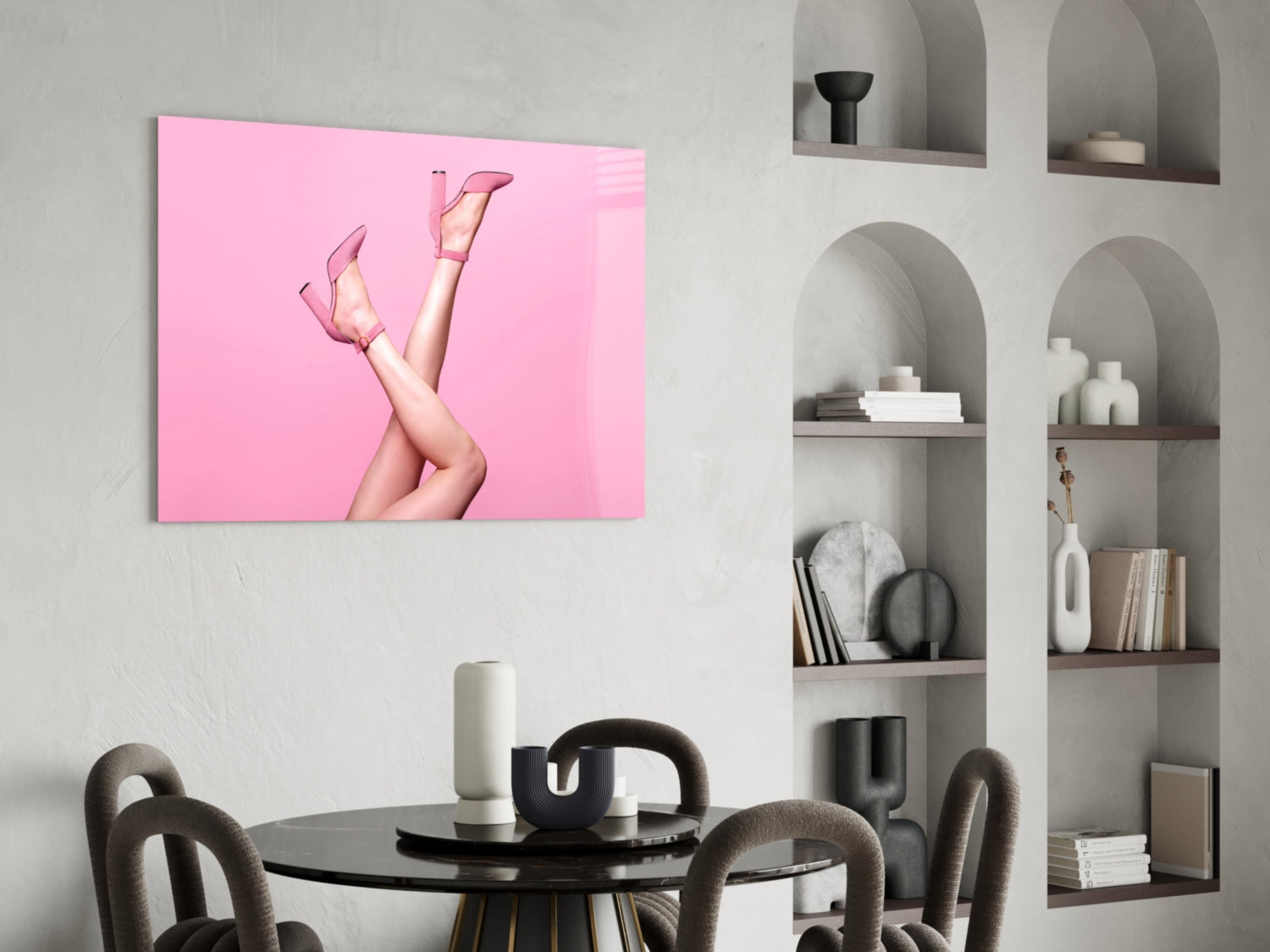 Pink glass wall art featuring legs in pink heels against bright pink background, displayed above black dining table in modern interior.