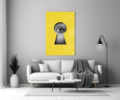 Yellow glass wall art with black keyhole cutout and eye illustration, displayed above white sofa in modern living room.