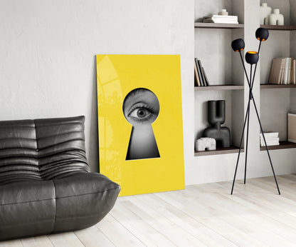 Bright yellow glass wall art featuring a grayscale eye peering through a keyhole, displayed in a modern living room setting.