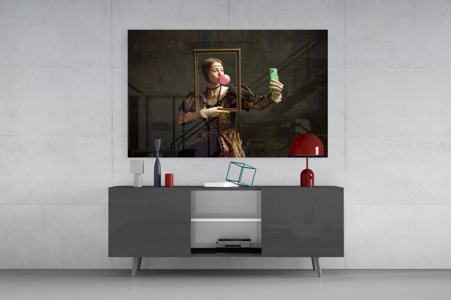 Modern living room display showing framed glass wall art of figure holding smartphone and blowing pink bubble above gray media console with red accents.