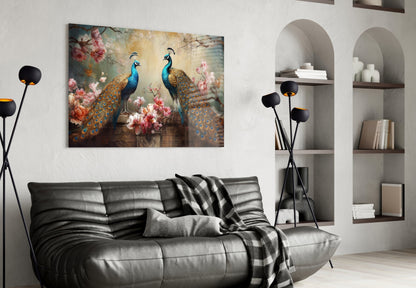Glass wall art depicting two ornate peacocks with blue heads and golden feathers among pink flowers, displayed above a black leather sofa in a modern living room.