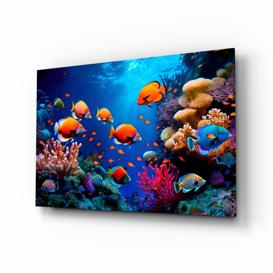 Angled display of glass wall art showing a vibrant underwater coral reef scene with orange fish and colorful corals against deep blue water.