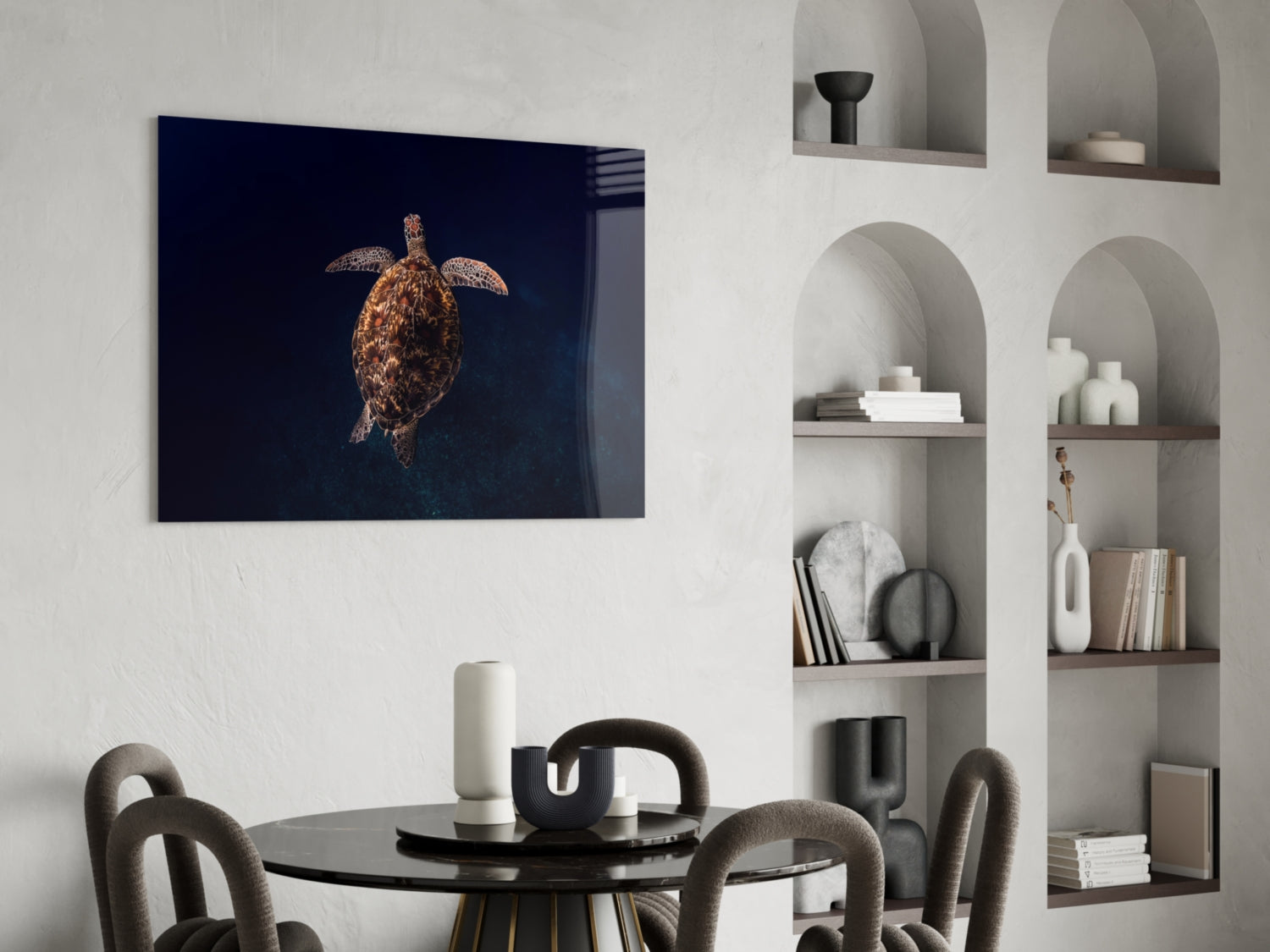 Sea turtle glass wall art with dark blue background displayed above a round black dining table in a modern interior with built-in shelving.