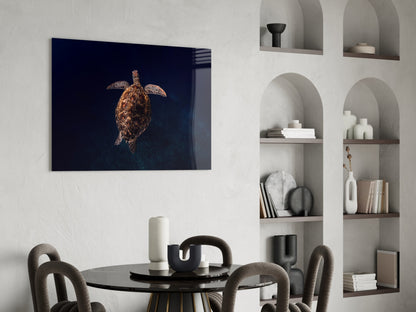 Sea turtle glass wall art with dark blue background displayed above a round black dining table in a modern interior with built-in shelving.