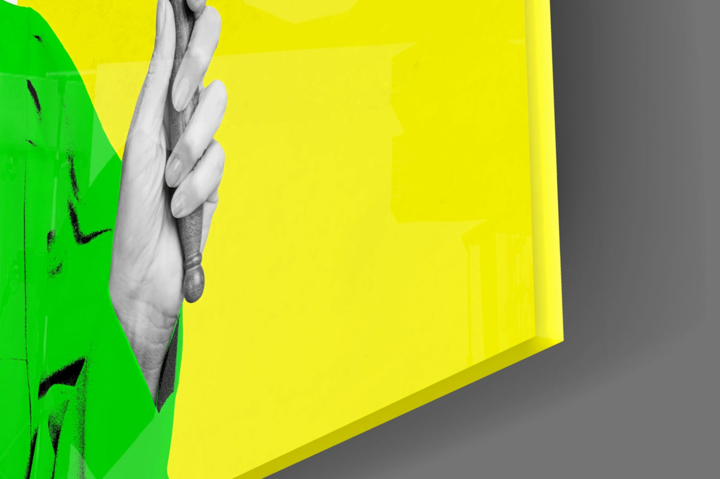 Close-up of colorful glass wall art with green and yellow panels, black brushstroke details, and a grayscale hand gripping the edge.