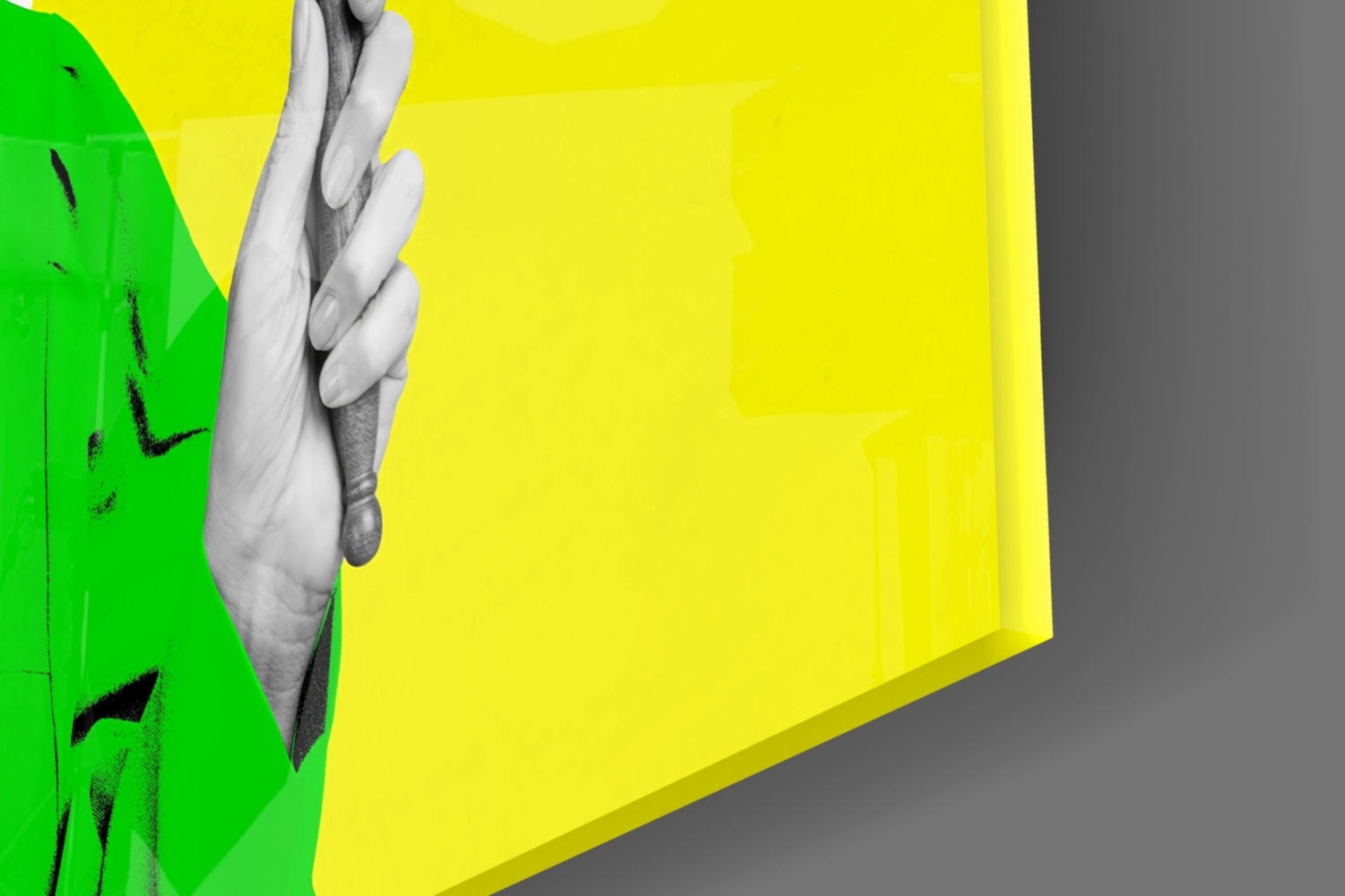 Close-up of colorful glass wall art with green and yellow panels, black brushstroke details, and a grayscale hand gripping the edge.