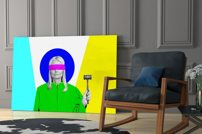 Colorful glass wall art featuring a woman in green jacket with pink blindfold and blue circular halo, holding gavel, displayed in modern living room with wooden chair.
