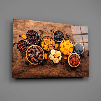 Overhead view of wooden board canvas displaying colorful dried fruits and nuts in ceramic bowls arranged in circular pattern against gray background.