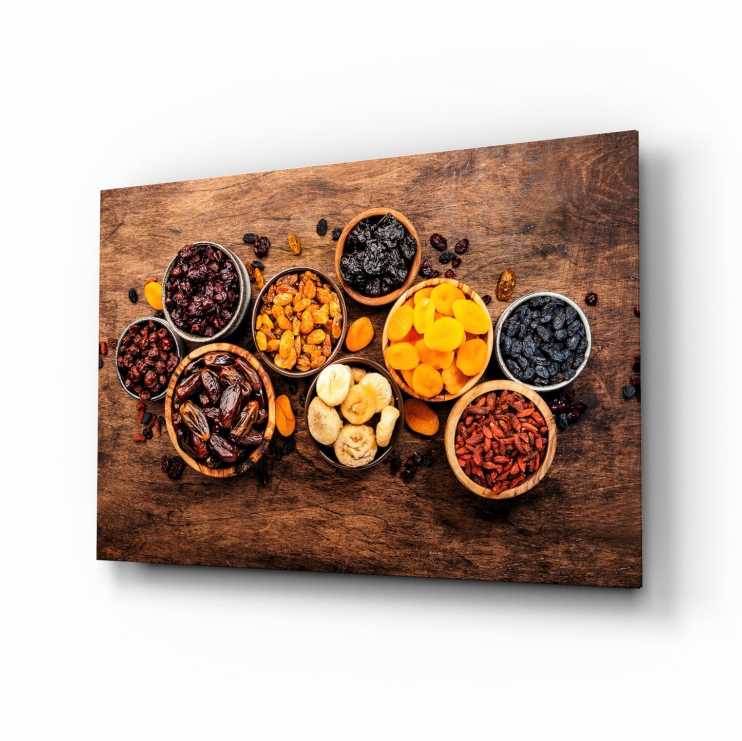 Angled perspective of wooden wall art displaying various dried fruits and nuts in ceramic bowls arranged on a textured brown wood surface.