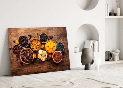 Canvas wall art leaning against white wall displays colorful dried nuts and fruits in wooden bowls on rustic brown background.
