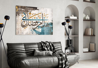 Modern living room interior with black leather sofa displaying Surah An-Naml glass wall art featuring Arabic calligraphy in blue, gold, and white tones above.