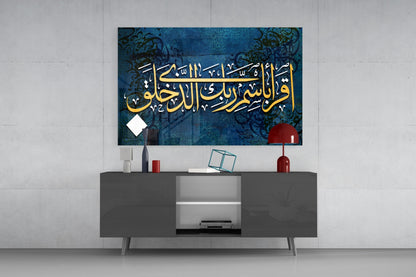 Blue glass wall art with gold Arabic calligraphy displayed above gray media console in modern interior setting.