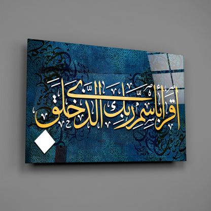 Angled view of blue glass wall art with gold Arabic calligraphy and geometric patterns, displayed against gray background.