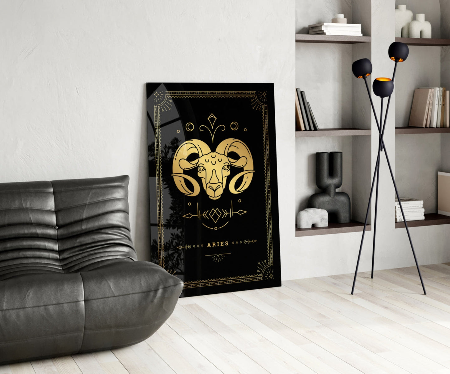 Black and gold Aries zodiac glass wall art displayed in modern living room with gray leather chair and wall shelving.
